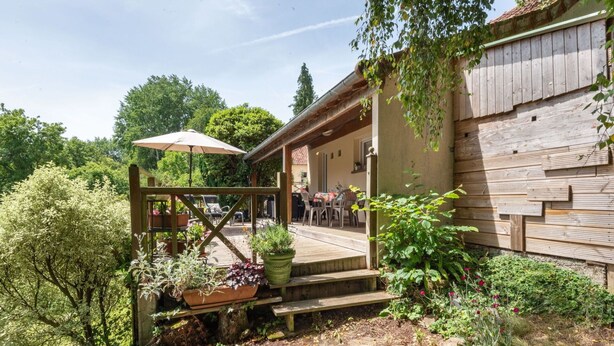 Un espace extérieur aménagé dans un style rustique, avec une terrasse en bois, une table couverte entourée de chaises et des plantes en pot.