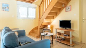 Un salon avec un canapé bleu, un téléviseur posé sur un meuble en bois, un escalier et une fenêtre avec des rideaux.