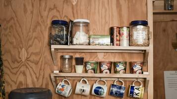 A wooden shelf with jars of granola and other food items, and mugs hanging below.