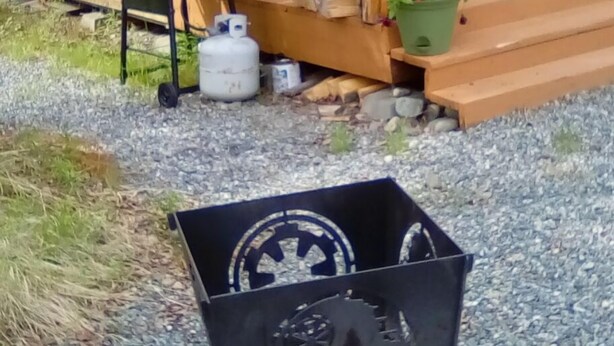 Una cabaña de madera con un porche, una parrilla, una silla y una planta en maceta.