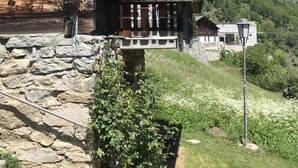 Un bâtiment rustique en bois, doté de fondations en pierre, d’une antenne parabolique et offrant une vue sur un paysage montagneux.