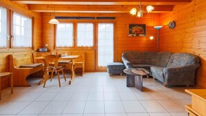 L’intérieur chaleureux d’un chalet avec des murs en bois, un coin repas comprenant une table et des chaises, un canapé et un luminaire au plafond.