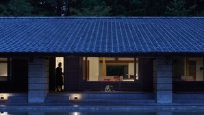 Een traditioneel Japans gebouw met een betegeld dak, een stenen fundering en een spiegelbeeld in het water ervoor.