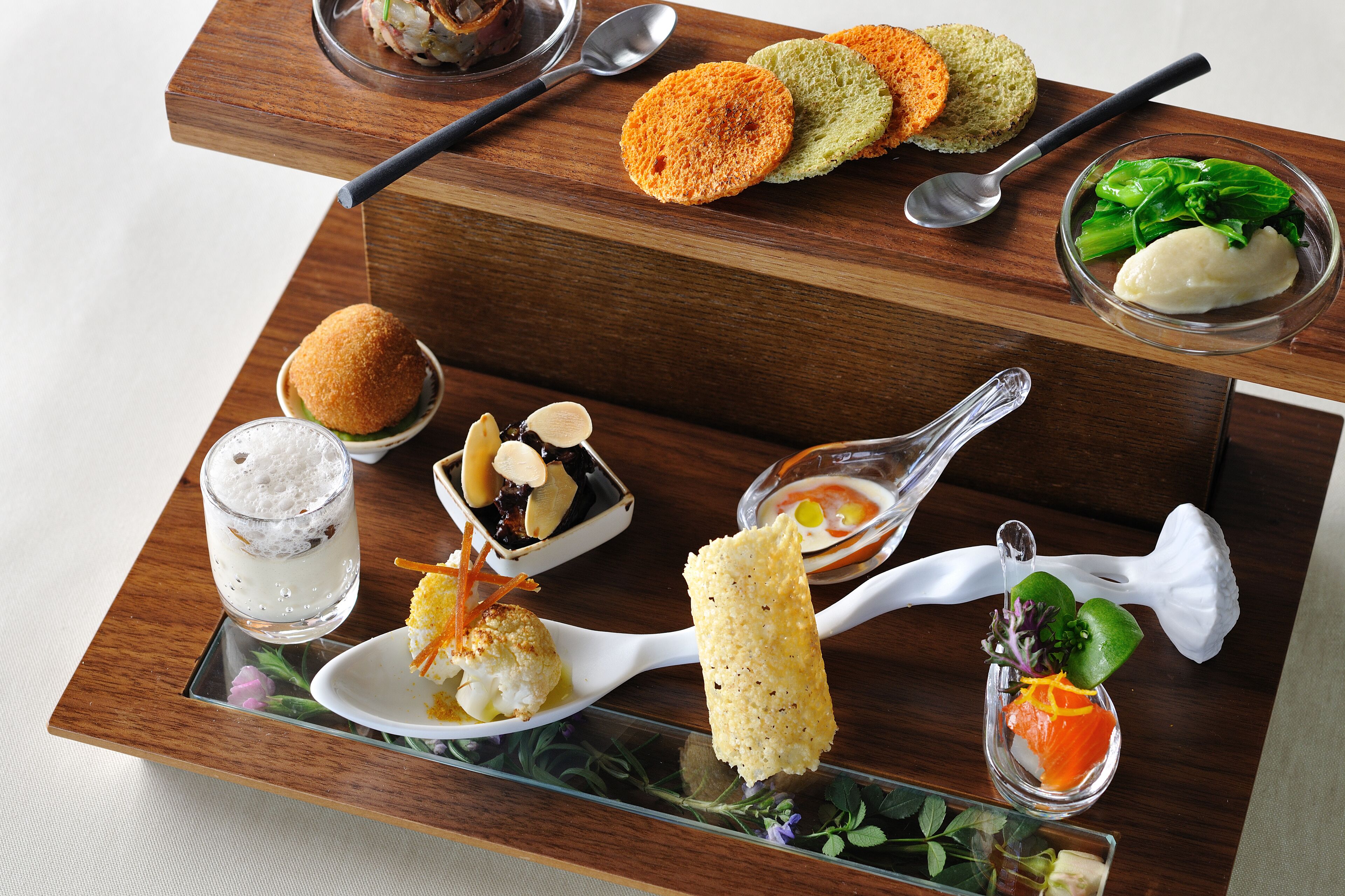 A wooden serving tray with various dishes including sushi, bread, and a glass of iced beverage.