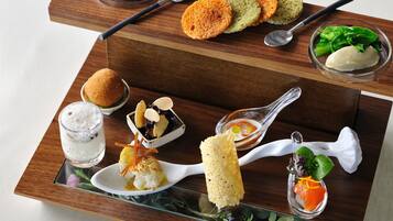 A wooden serving tray with various dishes including sushi, bread, and a glass of iced beverage.