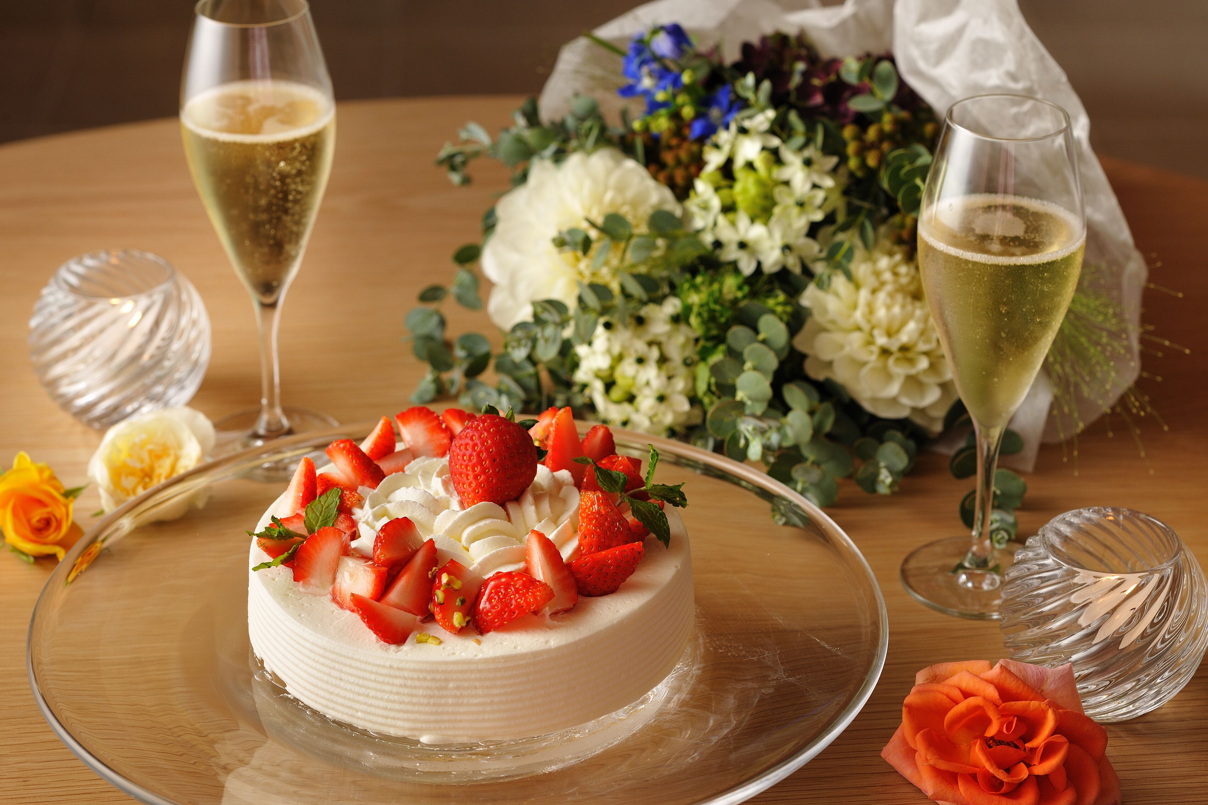 A cake with strawberries and cream, surrounded by flowers and champagne glasses on a table.