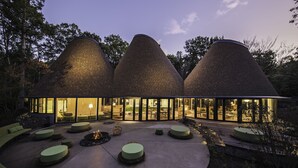 Een modern gebouw met drie kegelvormige daken, een ruim buitenterrein met ronde kussens en een vuurkorf.