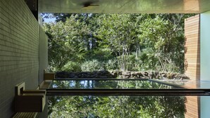 Een modern gebouw met een glazen atrium dat bomen en een rotsentuin weerspiegelt.
