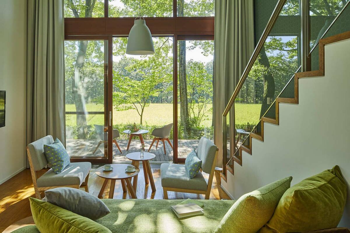 A modern interior with a staircase, large windows, and a seating area with a table and chairs.