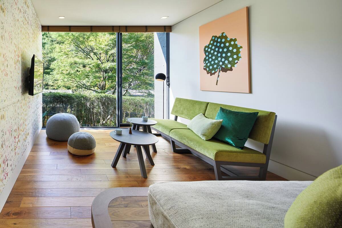 A modern living room with a green sofa, round coffee table, and two bean bags. A large window offers a view of greenery outside.