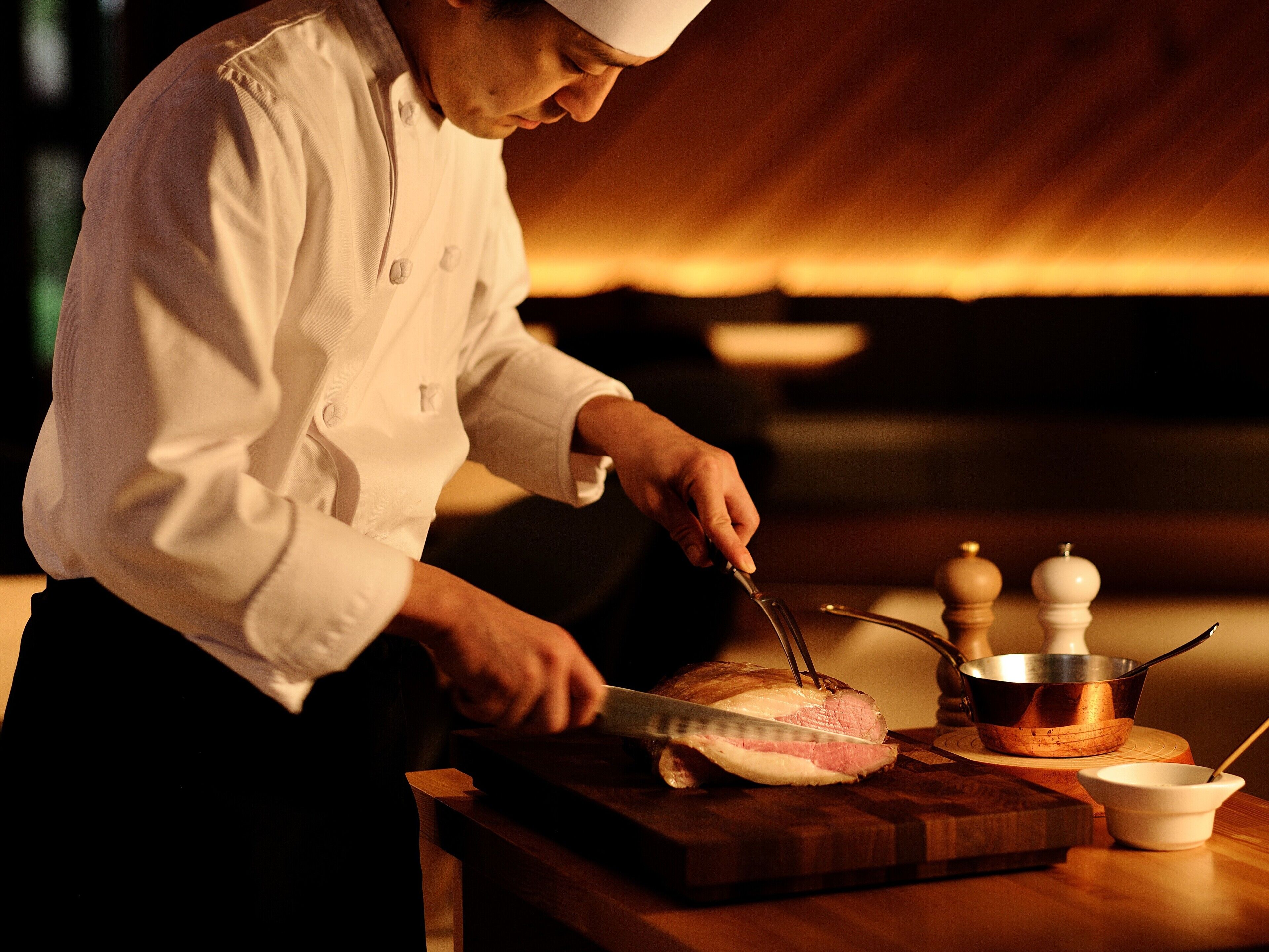 A chef slicing meat on a wooden cutting board in a kitchen setting.