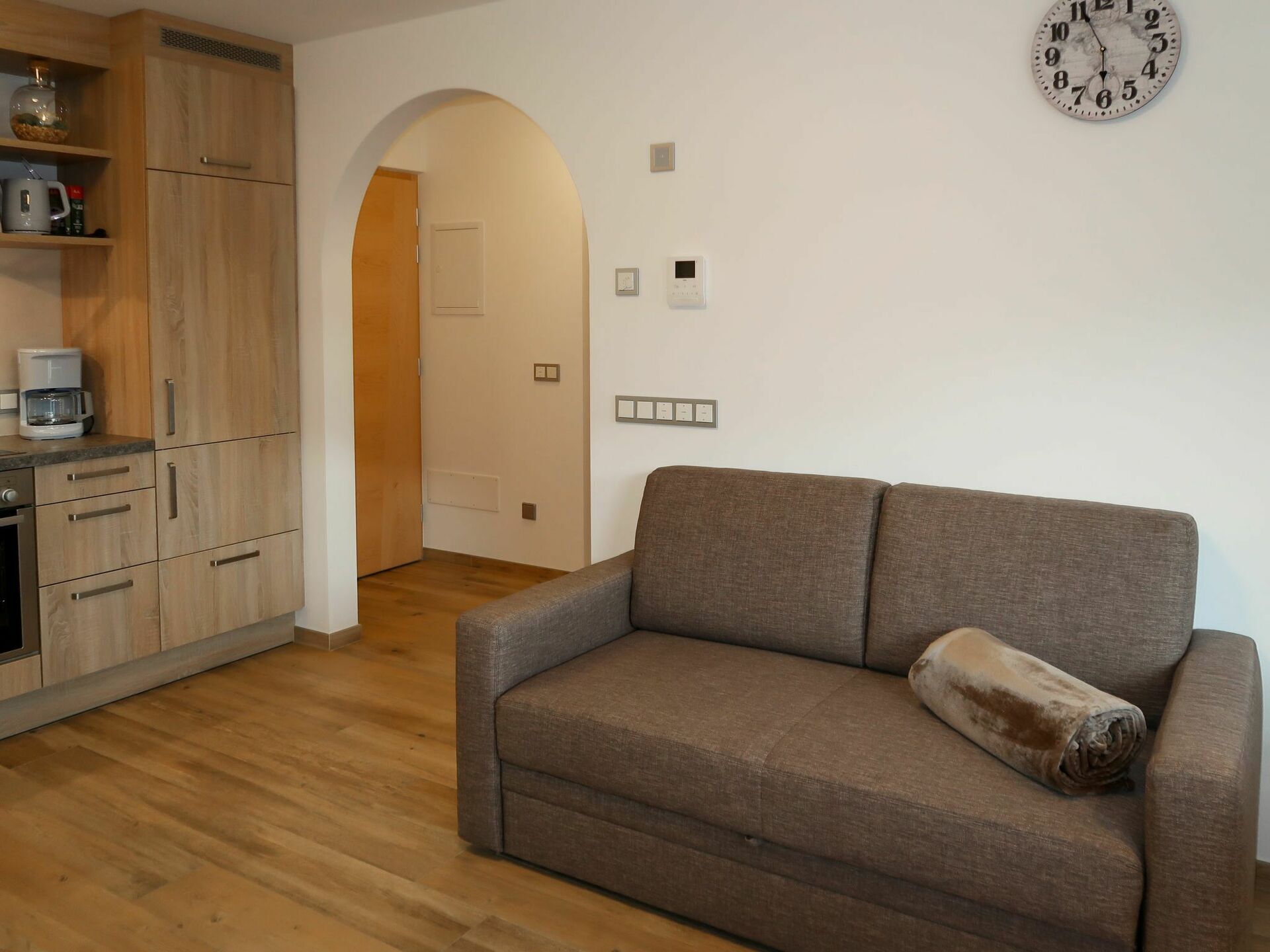 A modern living room with a sofa, a coffee machine, and a wall clock.