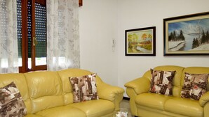 A living room with two yellow leather sofas, a small white round coffee table, and two framed paintings on the wall. - Nice apartment for 6 guests with WIFI, TV, patio and pets allowed (Eraclea)