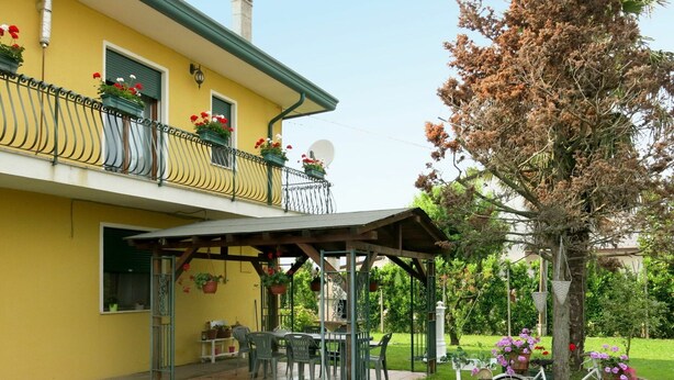 A yellow building with a balcony, a covered patio area, and a bicycle. - Nice apartment for 6 guests with WIFI, TV, patio and pets allowed (Eraclea)