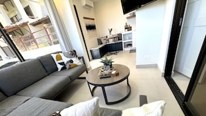 En moderne stue med en grå sofa, et rundt sofabord og et fjernsyn ophængt på væggen.
