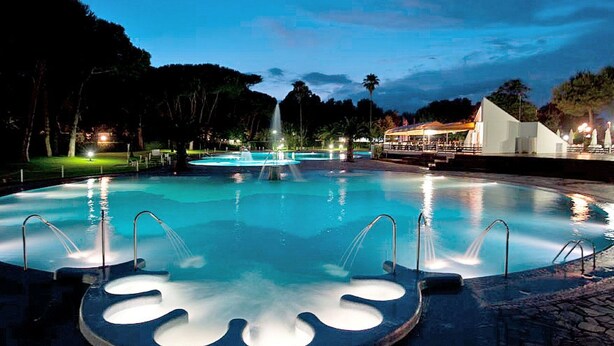 A swimming pool with a fountain, surrounded by trees and a building with outdoor seating. - Nice apartment in villa for 5 guests with WIFI, pool, A/C, TV and terrace (Cellole)