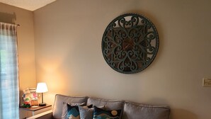 Un salon avec un canapé gris, des coussins décoratifs, une œuvre d’art murale, une lampe et une petite table sur laquelle se trouve une télécommande.