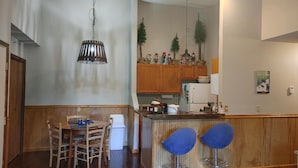 Une cuisine avec des meubles de rangement en bois, une table à manger avec des chaises et un coin bar avec des tabourets.