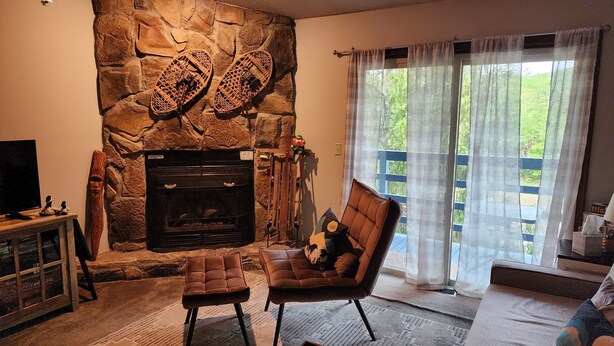 Un salon avec une cheminée en pierre, un canapé, une table basse et une grande fenêtre avec des rideaux.