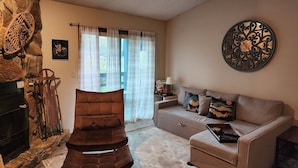 Un salon doté d’une cheminée en pierre, d’un fauteuil marron à coussins moelleux, d’un canapé avec des coussins à motifs et d’un élément décoratif mural.