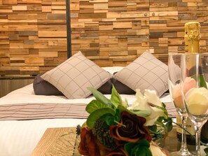 A neatly made bed with two pillows, a vase with flowers, and two wine glasses on a table. - Hotel Venus Garden - Adults Only (Nagoya)