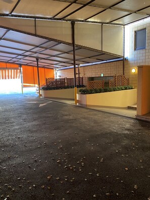 A covered parking area with a concrete floor, metal railings, and a brick wall. - Hotel Venus Ritz - Adults Only (Seto)
