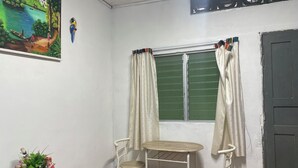Una habitación con ventana, dos sillas, una mesita pequeña, un jarrón decorativo y un cuadro en la pared.