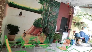 Una habitación con un mural de una escena boscosa, sillas verdes y plantas en macetas.