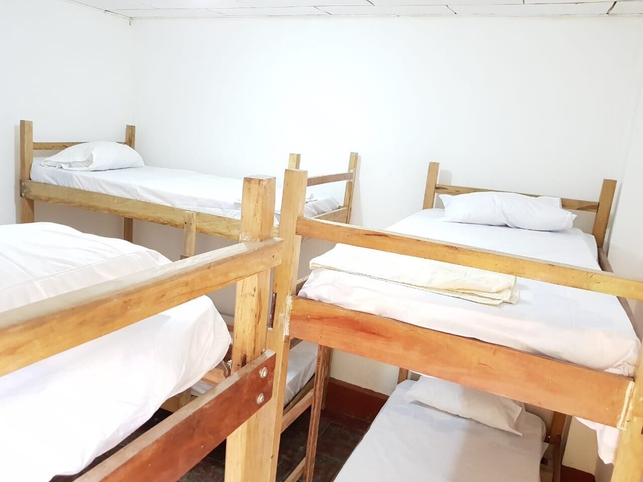 A dormitory room with four wooden bunk beds, each with white bedding.