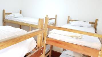 A dormitory room with four wooden bunk beds, each with white bedding.