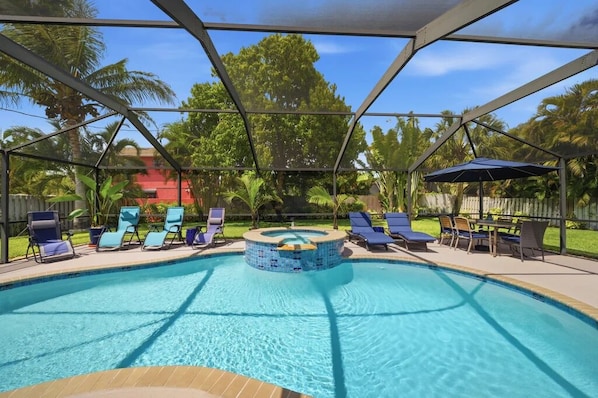 A swimming pool with lounge chairs and a hot tub, surrounded by palm trees and a fenced area.