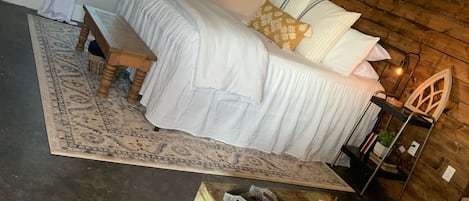 Relax in this serene bedroom with a large bed, a wooden bench, and a small table with a lamp.