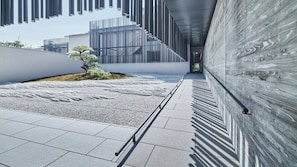 Stroll through a serene outdoor space, bordered by a low wall and a modern architectural element, featuring a tranquil landscaped area with a bonsai tree.