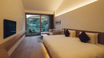 Quarto de hotel moderno com uma cama grande, um sofá, uma TV e vista para uma paisagem montanhosa pela janela.