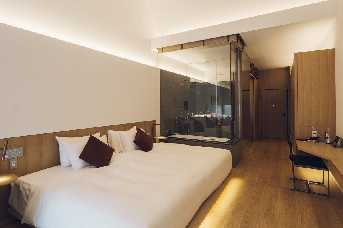 A hotel room with a large bed, a desk, a mirror, and a shower area.