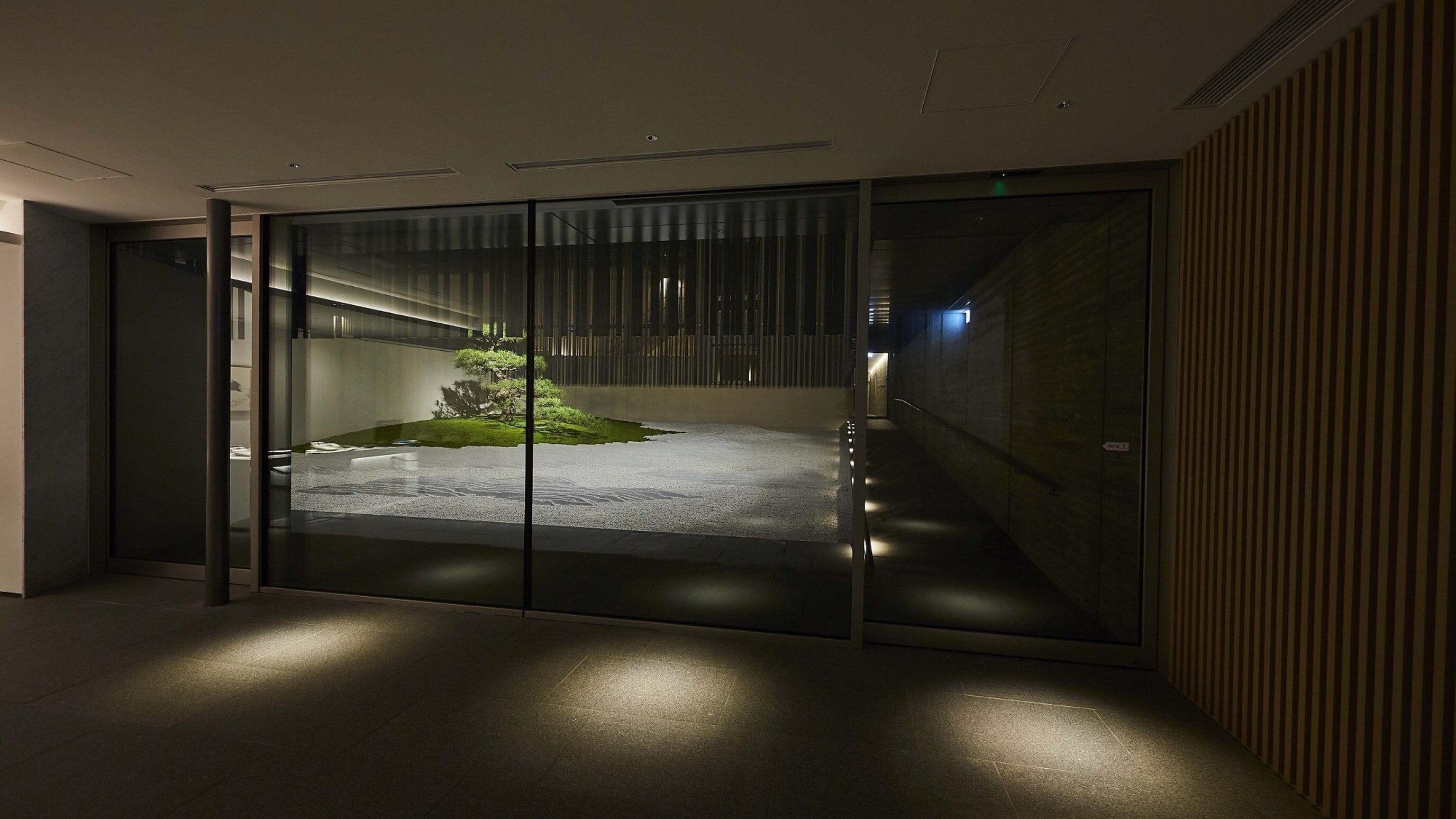A modern interior with a glass partition, a small indoor garden, and a staircase.