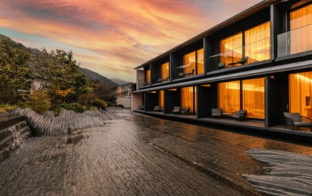 A modern building with multiple balconies and large windows, surrounded by a wet cobblestone path.