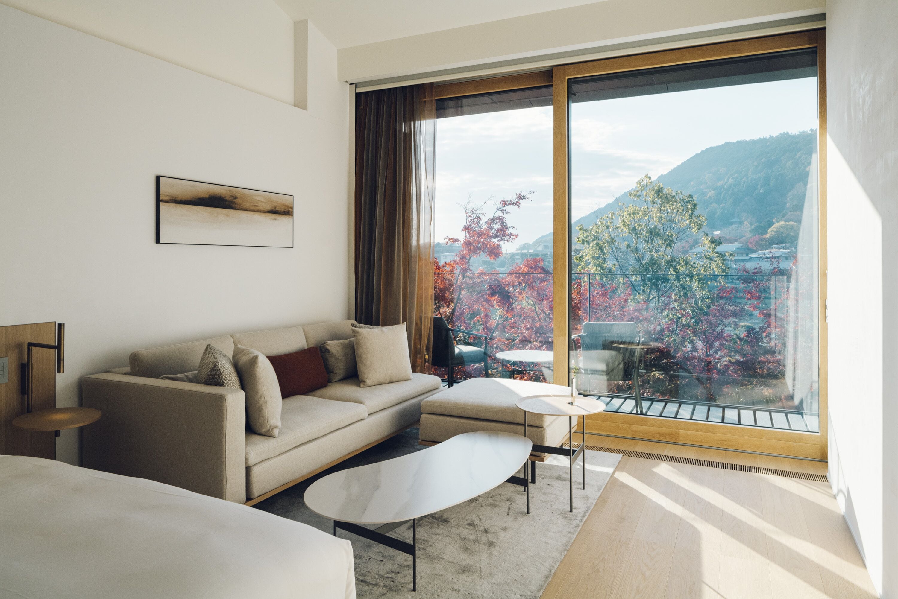 Una habitación de hotel moderna con un ventanal grande, un sofá, una mesita y una cama.