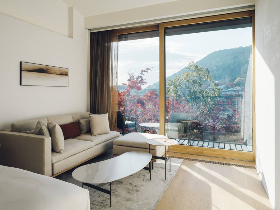 Una habitación de hotel moderna con un ventanal grande, un sofá, una mesita y una cama.