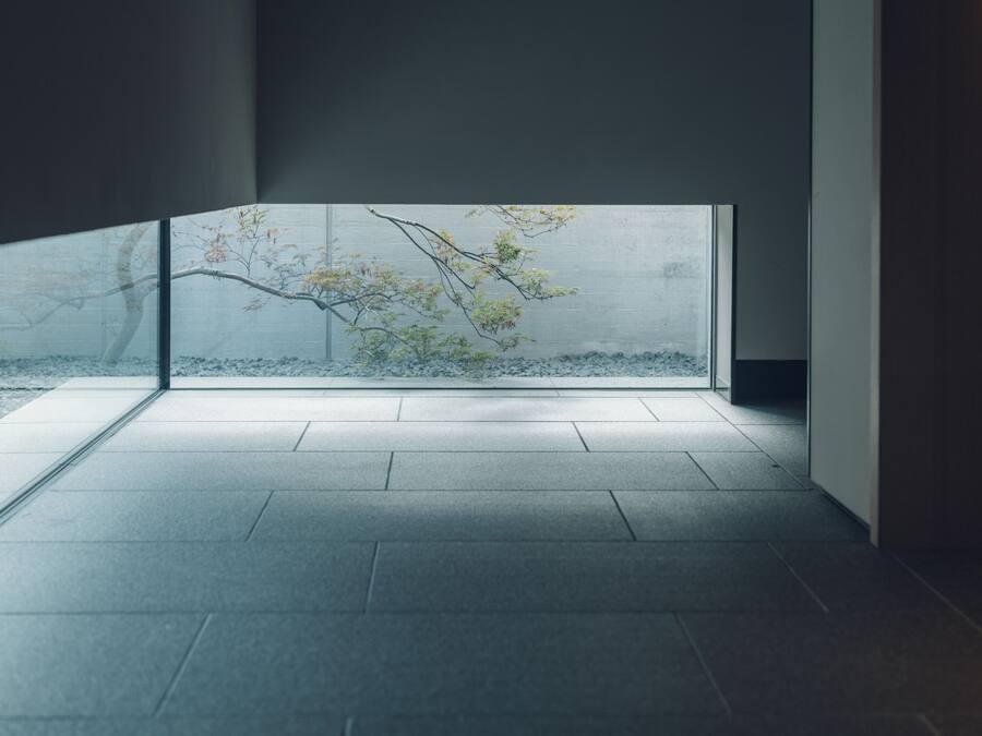 Un interior moderno con un amplio ventanal, suelo de baldosas y vista a un árbol.