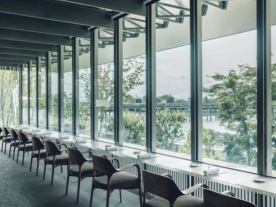 A conference room with large windows, rows of chairs, and a view of a bridge and trees.