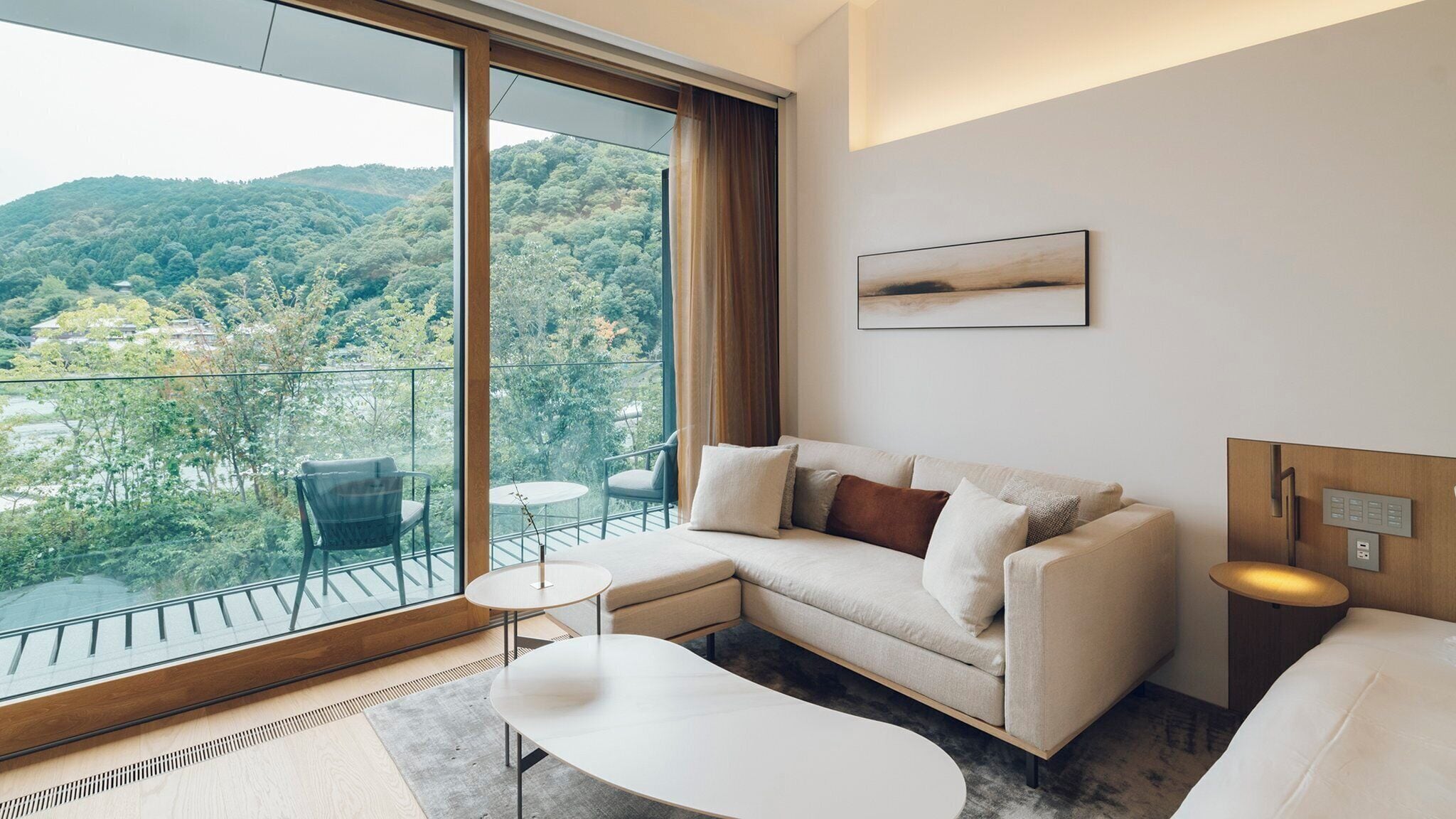 A modern hotel room with a large balcony, a sofa, a small table, and a painting on the wall.
