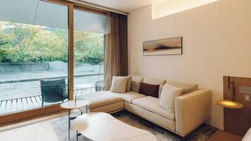 A modern hotel room with a large window, a sofa, a small table, and a wooden floor.