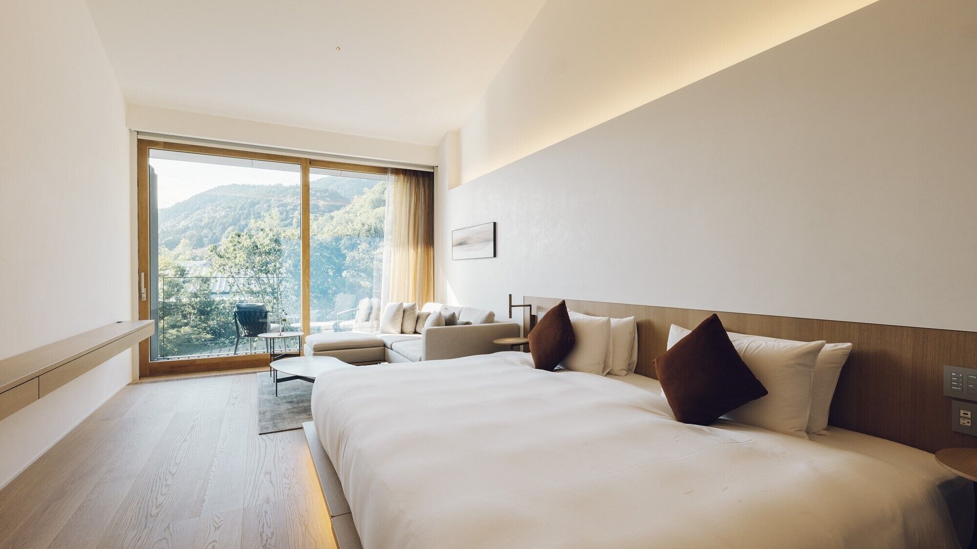 A hotel room with a large bed, a sofa, a small table, and a view of the outdoors.