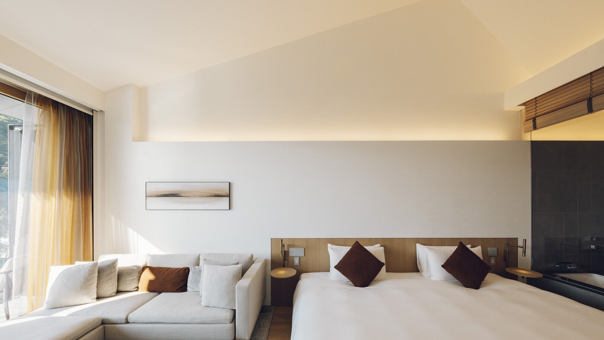 A hotel room with a bed, a sofa, a bedside table, a nightstand, and a window with curtains.
