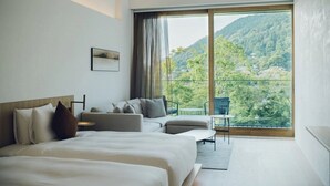 A modern hotel room with a large bed, a sofa, a small table, and a balcony with a view of a forested mountain. - MUNI KYOTO (Kyoto)