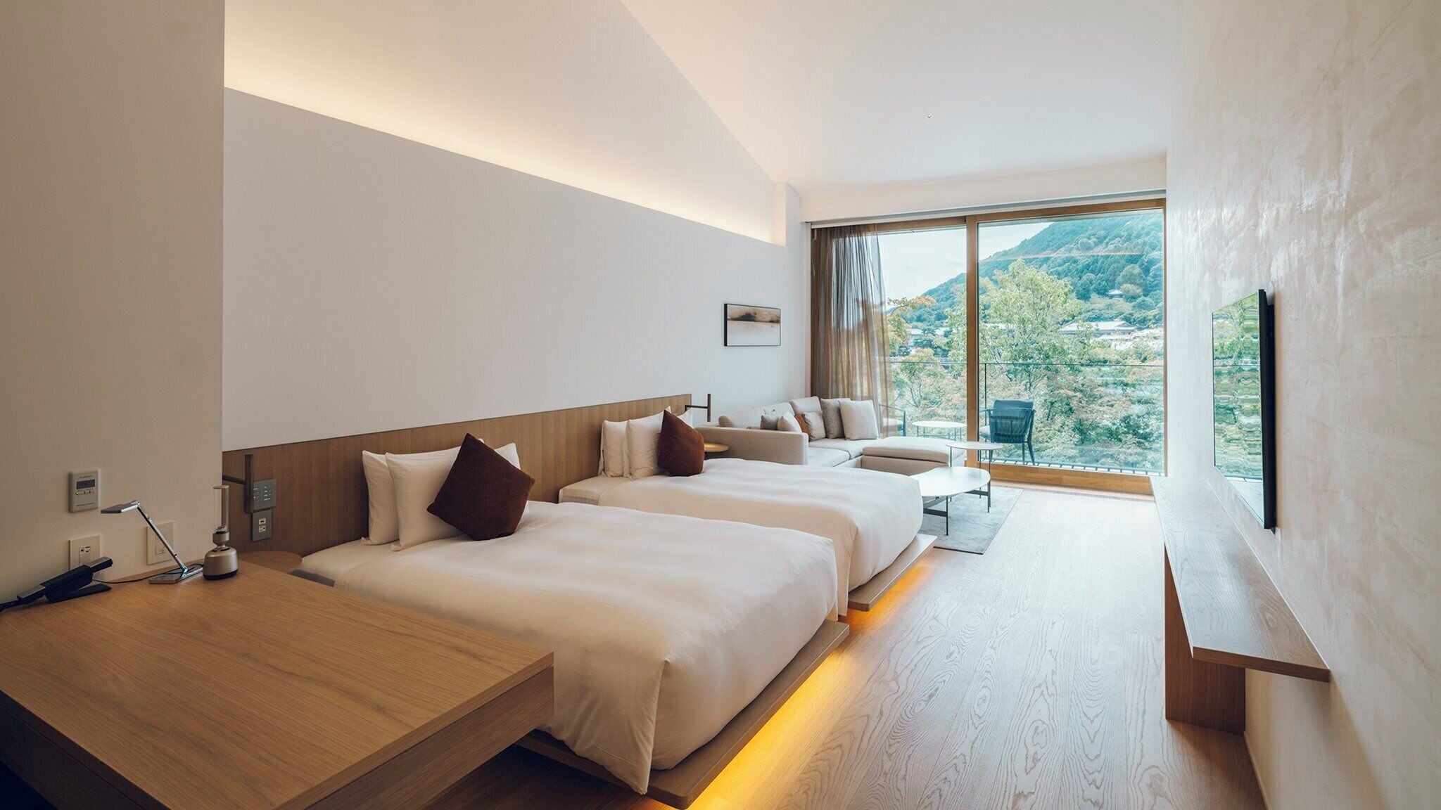 Quarto de hotel moderno com duas camas, uma escrivaninha e uma janela grande com vista para o exterior.