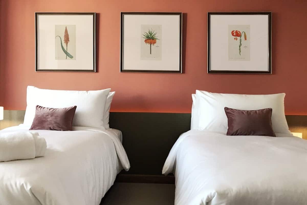 Hotellihuone, jossa on kaksi sänkyä, valkoiset vuodevaatteet ja seinällä kolme kehystettyä kasvitieteellistä kuvaa.