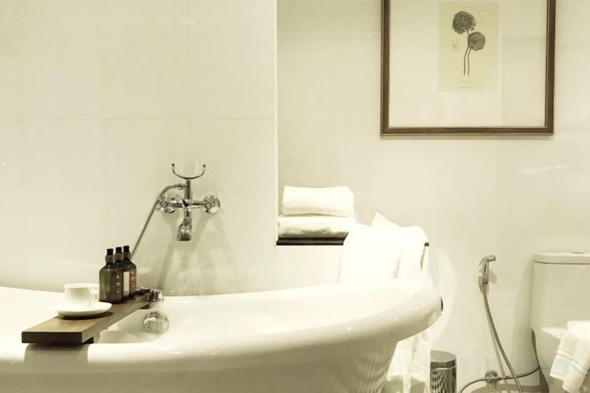 A bathroom with a bathtub, a shower, and a toilet. There is a towel rack with towels and a framed picture on the wall.