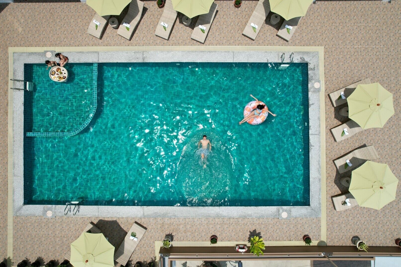 Vista aérea de una piscina rectangular con sillas de descanso y sombrillas alrededor.